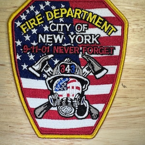 May include: Embroidered patch featuring the words "Fire Department City of New York" and "9-11-01 Never Forget" over a design of the American flag. The patch includes a firefighter's helmet, axes, and a gas mask.