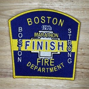 May include: A blue and yellow embroidered patch with the text "Boston Strong 129th Marathon Finish Fire Department".
