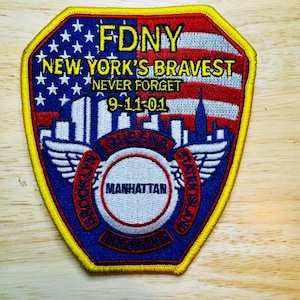 May include: Embroidered FDNY patch with a patriotic design. Features the American flag, the New York City skyline, and the text "NEW YORK'S BRAVEST NEVER FORGET 9-11-01." Includes the names of NYC boroughs: Brooklyn, Queens, Manhattan, Bronx, and Staten Island.