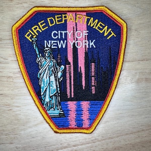 May include: A blue and yellow embroidered patch with the text "Fire Department City of New York". The patch features a depiction of the Statue of Liberty and the New York City skyline.