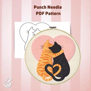 May include: Punch needle PDF pattern featuring a heart-shaped design with two cats embracing. One cat is orange tabby, the other is black. The design is in a wooden embroidery hoop, with a line drawing of the design on a white paper.