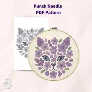 May include: Punch needle pattern for a cat face made of purple flowers. The pattern is in a hoop and includes a gray and white color scheme.