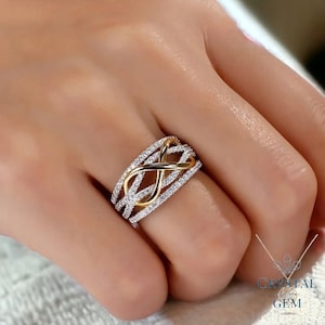 May include: A gold and silver infinity ring with a band of pave set diamonds. The ring is on a hand.