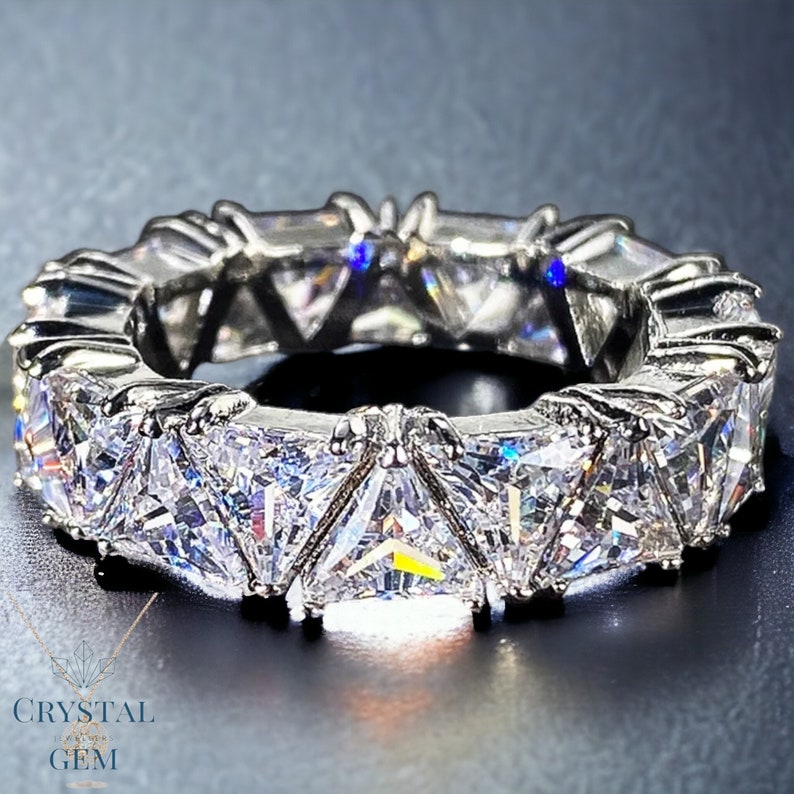 May include: A silver eternity band ring with a row of triangular-shaped clear cubic zirconia stones.
