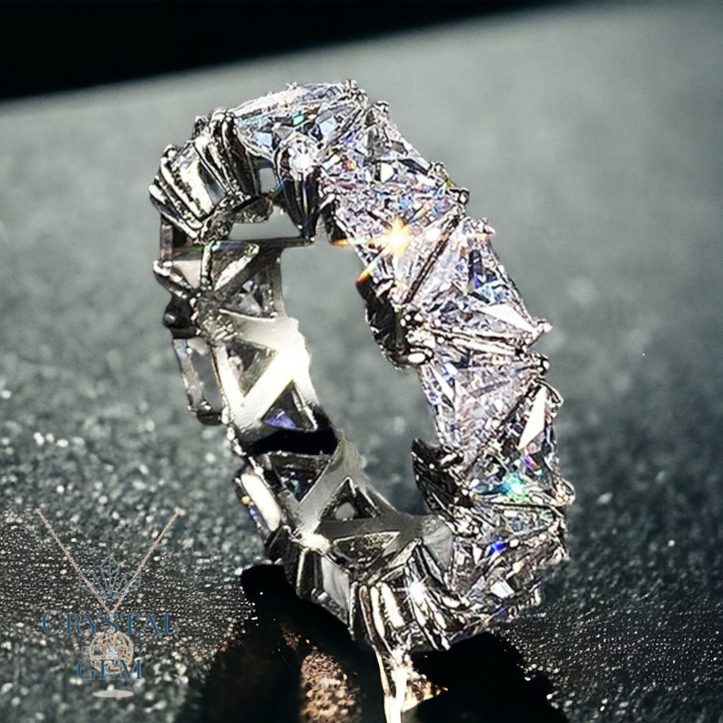 May include: A silver ring with a row of triangular-shaped clear stones set in a geometric pattern.