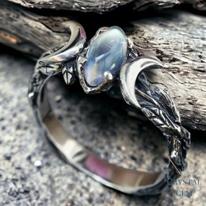 Könnte beinhalten: Ein silberner Ring mit Mond- und Ast-Design. Der Ring verfügt über einen großen, schillernden Opal-Edelstein.