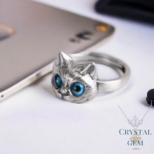 May include: A silver ring with a cat face design. The cat has large blue eyes and a detailed face.
