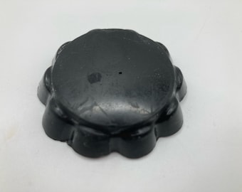 May include: A black, flower-shaped object with a slightly textured surface. The object has a series of rounded petals around its edge. The item is likely a decorative piece or a functional item.