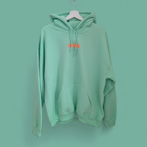 Può includere: Una felpa con cappuccio verde chiaro con un piccolo logo ricamato arancione che dice "DR. WOW".