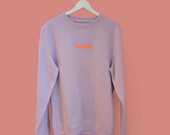 Puede incluir: Una sudadera de color lavanda con mangas largas y cuello redondo. La sudadera tiene la palabra "WHATEVER" impresa en naranja en la parte delantera.
