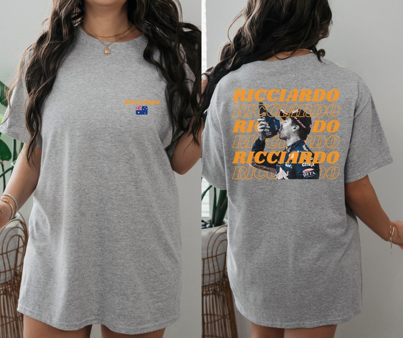 May include: Grey t-shirt featuring a graphic of a racing driver drinking from a bottle. The graphic is repeated several times and the text "RICCIARDO" is printed in orange. The shirt also has a small Australian flag printed on the front.