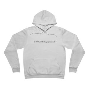 May include: A white long-sleeve hooded sweatshirt featuring a front kangaroo pocket and a drawstring hood. The center of the chest displays the black printed text "Look Who's Monkeying Around!!" in a simple, dark, sans-serif typeface.