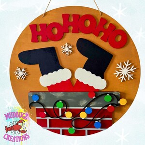 May include: A round wooden Christmas sign with the words "HO HO HO" in red. Santa's legs and boots are seen coming out of a chimney with colorful lights. Snowflakes and a logo are also present.