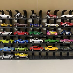 May include: A black metal display shelf with multiple tiers holds a collection of miniature toy cars in various colors, including red, blue, green, yellow, and black.