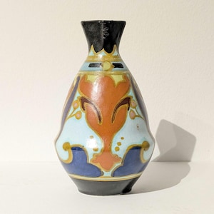 May include: A decorative ceramic vase with a black rim and base. The vase features a light blue body with orange, brown, and gold floral designs. The vase is approximately 15 cm tall.