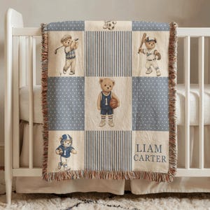 May include: A baby blanket with a patchwork design featuring teddy bears playing sports. The squares alternate between blue polka dots, blue stripes, and images of bears playing golf, baseball, basketball, soccer, and football. The name "LIAM CARTER" is printed on the bottom right.