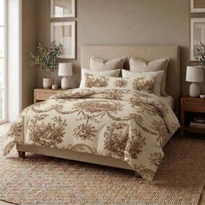 May include: A beige and brown toile bedding set on a bed. The set includes a comforter, pillowcases, and decorative pillows. The comforter and pillowcases feature a detailed pastoral scene design. The bed is in a neutral-toned bedroom with matching decor.