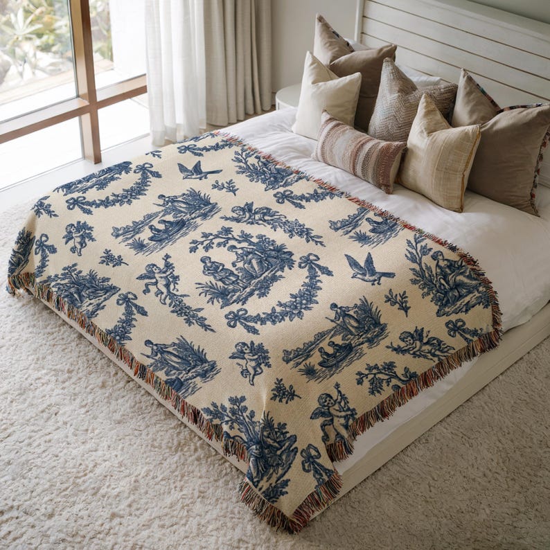 Blue toile woven blanket featuring cherubs, pastoral countryside scenes, and floral garlands in French country farmhouse style.