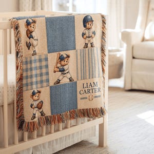 May include: A woven throw blanket featuring a grid pattern of blue and beige squares. The design includes illustrations of teddy bears dressed in baseball uniforms, along with the text LIAM CARTER and a baseball graphic. The edges have fringe.
