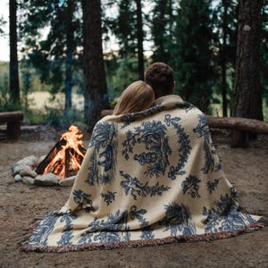 Blue toile woven blanket featuring cherubs, pastoral countryside scenes, and floral garlands in French country farmhouse style.