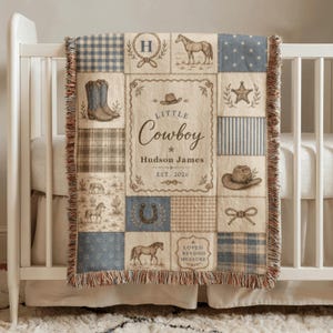 May include: A woven throw blanket featuring a patchwork design in shades of blue, beige, and cream. The pattern includes illustrations of horses, cowboy boots, hats, stars, and lassos. The centre text reads Little Cowboy, Hudson James, EST. 2026.