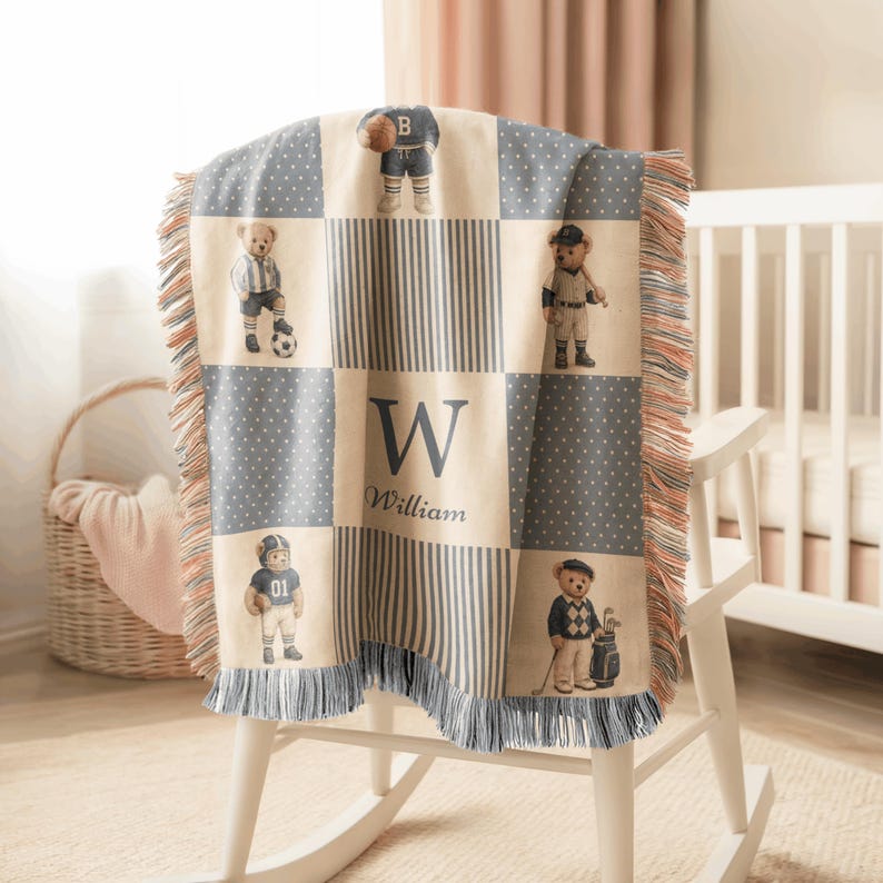 May include: A woven throw blanket featuring a checkered pattern of cream and blue-grey panels. The design includes illustrations of teddy bears dressed in various sports uniforms, the letter W, and the name William in a dark blue script font.