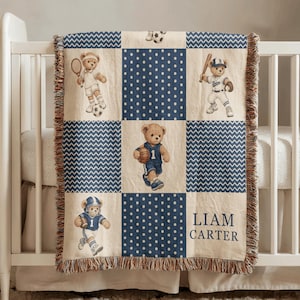 May include: A woven throw blanket featuring a grid pattern of cream and navy blue squares. The design includes illustrations of teddy bears playing tennis, baseball, football, and basketball, alongside navy blue polka dots and chevron stripes.
