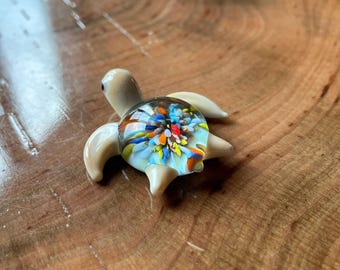 Op de afbeelding: Een klein glazen zeeschildpad beeldje met een kleurrijk, veelkleurig, confetti-achtig ontwerp in de schelp.