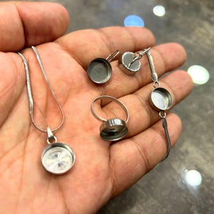 Può includere: Una collana a catena d'argento con un ciondolo rotondo, un anello d'argento con una montatura rotonda e un braccialetto d'argento con un ciondolo rotondo. Tutti i pezzi di gioielleria hanno una finitura argentata e sono in metallo.