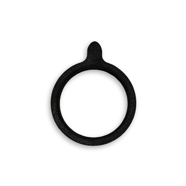 May include: A circular black gasket with a textured surface and a small, rounded tab extending from the top edge. The object features a hollow center and a consistent, uniform thickness throughout its entire ring-shaped structure.