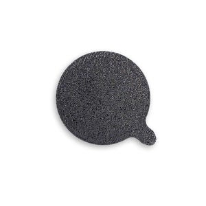 May include: A circular, dark gray, textured abrasive disc featuring a small, protruding tab on the lower right side. The surface has a coarse, granular appearance with a uniform dark charcoal color throughout the entire round shape.