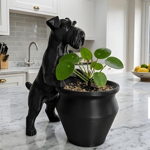 May include: A black dog-shaped sculpture leans over a black potted plant with round green leaves. The sculpture and plant are on a white marble countertop in a kitchen setting. The dog sculpture has a glossy finish.