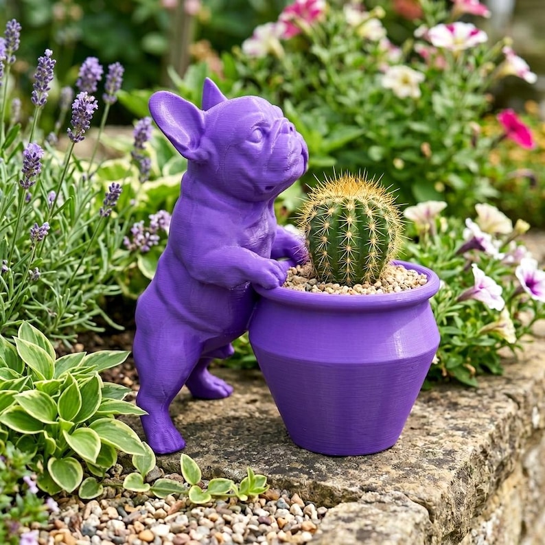 May include: A bright purple French bulldog figurine standing on its hind legs with its front paws resting on the rim of a matching purple flower pot. Inside the pot sits a small, round, green cactus with sharp, light-colored spines.