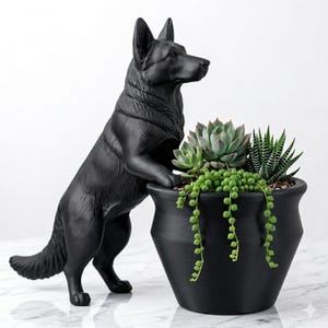 May include: A matte black German Shepherd figurine standing on its hind legs with its front paws resting on the rim of a matching matte black planter. The planter contains a variety of green succulents, including a string of pearls plant.