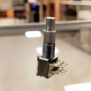 Könnte beinhalten: Ein silberner Drehschalter mit einem runden Knopf und sechs Stiften. Der Schalter ist für elektronische Schaltungen ausgelegt.