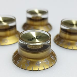 May include: Four gold guitar knobs with clear plastic tops. The knobs have white numbers and the word "VOLUME" is printed on one of the knobs.
