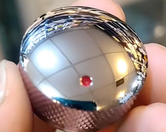 May include: A shiny silver metal knob with a textured surface and a reflective finish. The knob is round and has a slight dome shape.