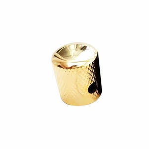 Könnte beinhalten: Ein goldfarbener Gitarrenknopf mit strukturierter Oberfläche. Der Knopf hat eine zylindrische Form mit flacher Oberseite und einem kleinen Loch an der Seite. Die Oberfläche hat ein Rautenmuster.