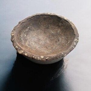 May include: A small, round, brown stone bowl with a rough, uneven texture.