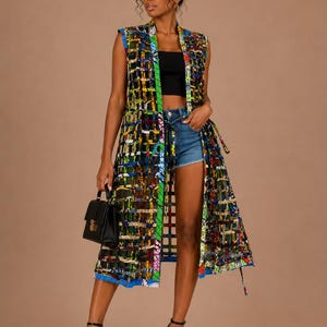 Puede incluir: Un chaleco largo sin mangas hasta la rodilla con un vibrante patrón de cuadrícula multicolor con acentos en azul, verde, amarillo y rojo. La prenda tiene un cuello estructurado, un diseño frontal abierto con un lazo en la cintura y dobladillo recto.