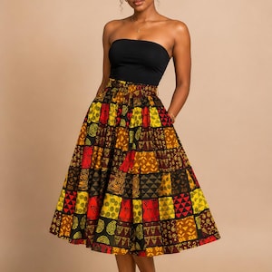 May include: A black strapless top paired with a high-waisted midi skirt featuring a vibrant patchwork pattern of red, yellow, and brown geometric shapes. The outfit includes a matching fabric headwrap with a bow detail and black heeled sandals.