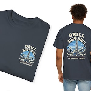 Puede incluir: Una camiseta azul oscuro con un gráfico de una plataforma de perforación y el texto "Drill Baby Drill Geothermal Energy" en la parte posterior.