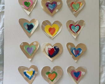 May include: A white background with twelve layered paper hearts in various colors, including pink, green, blue, yellow, orange, and red. The hearts are arranged in four rows of three. The word "Yay" is written in cursive in the bottom right corner.