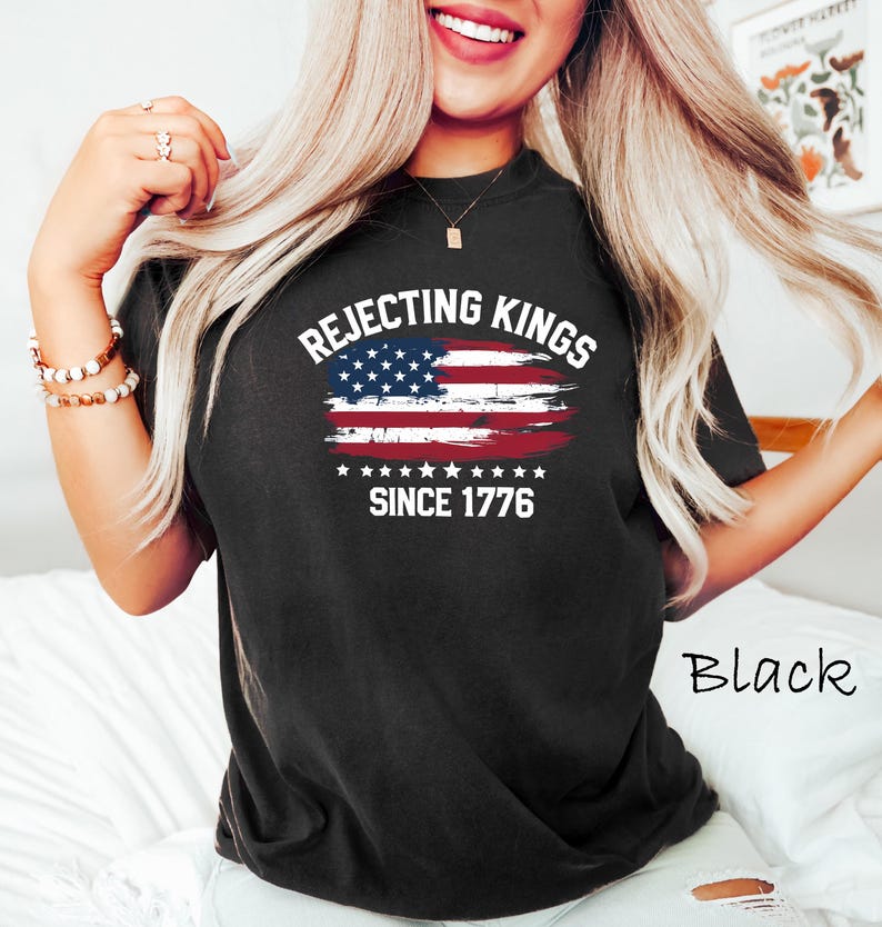 May include: Black t-shirt with the text "Rejecting Kings Since 1776" and a distressed American flag design. The shirt is a crew neck and has short sleeves. The word "Black" is written in cursive on the bottom right.
