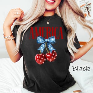 May include: Black t-shirt with a red, white, and blue cherry design and the word "AMERICA" printed on the front.