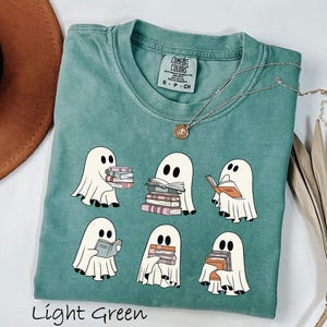 May include: Light green t-shirt featuring a design of six cartoon ghosts reading books. The ghosts are white with black eyes and are holding stacks of books. The text "Light Green" is at the bottom of the shirt.