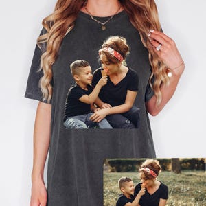 May include: Dark gray t-shirt featuring a photo of a woman and child sharing an ice cream cone. The image on the shirt shows the woman wearing a red and white headband. The word "Pepper" is written in cursive at the top right.