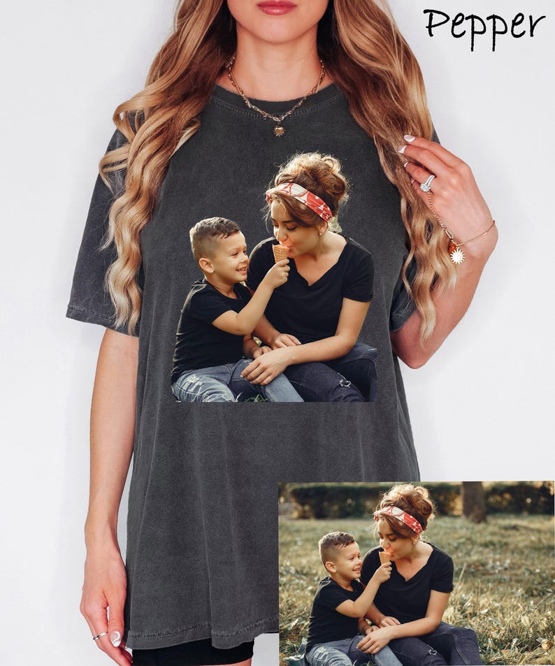 May include: Dark gray t-shirt featuring a photo of a woman and child sharing an ice cream cone. The image on the shirt shows the woman wearing a red and white headband. The word "Pepper" is written in cursive at the top right.