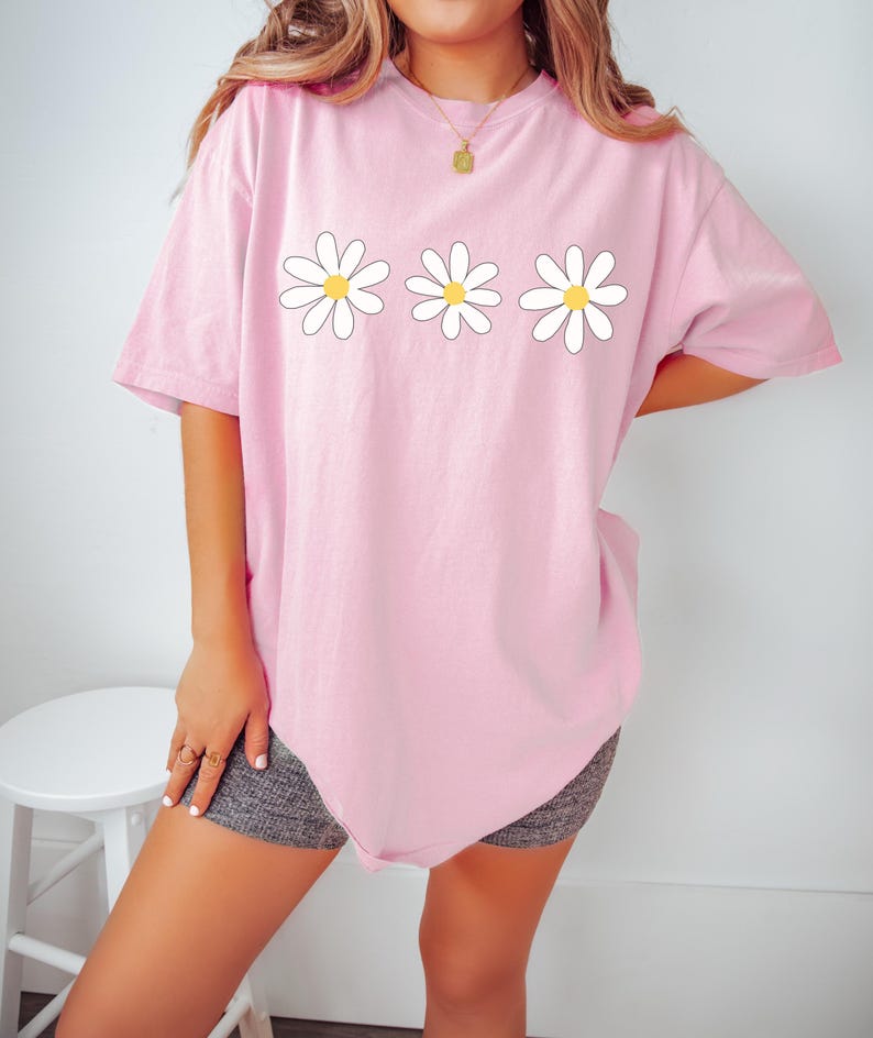 May include: A pink oversized t-shirt with a graphic of three white daisies with yellow centers.