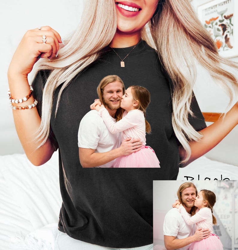 May include: Black t-shirt featuring a printed image of a man and a young girl. The image shows the man embracing the girl, who is kissing his cheek. The girl is wearing a pink tutu.